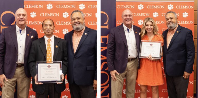 Graduates stand while holding diploma and smiling with school officials.
